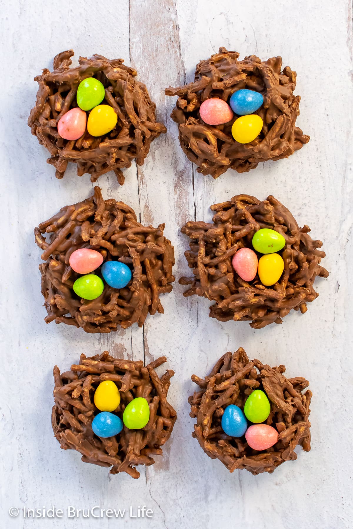 Six chocolate birds nest cookies with candy eggs in them.