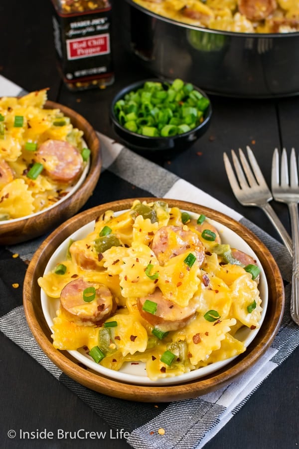 A white plate filled with cheesy pasta on a black and white towel and a pan of pasta in the background