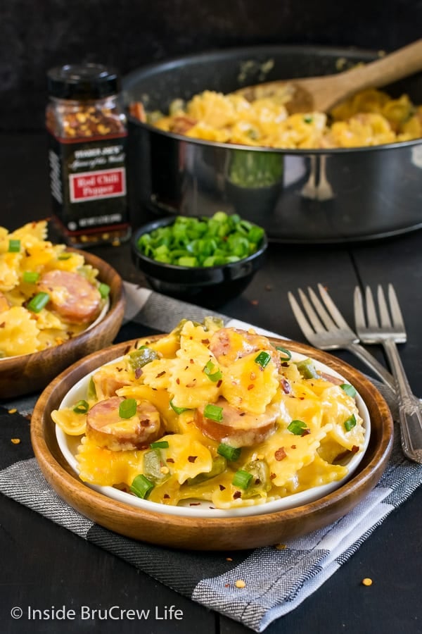 Plate of cheesy pasta on a black and white towel with a pan of pasta behind it