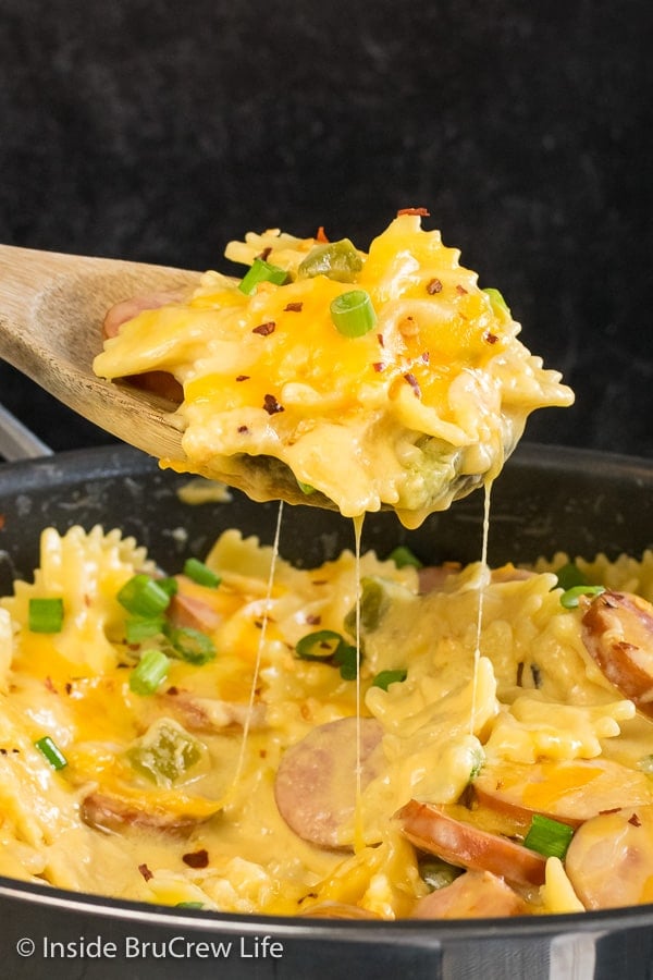 A scoop of cheesy pasta lifted up above the skillet filled with pasta