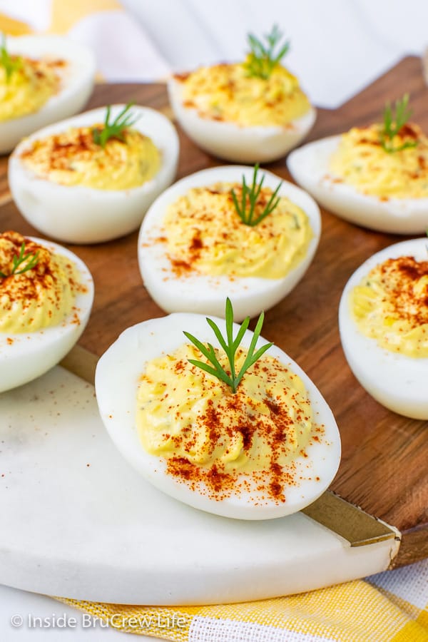 Close up picture of deviled eggs with dill and paprika on a white and brown tray