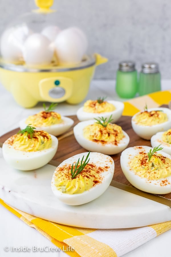 A tray with deviled eggs on it in front and a Dash egg cooker in the background