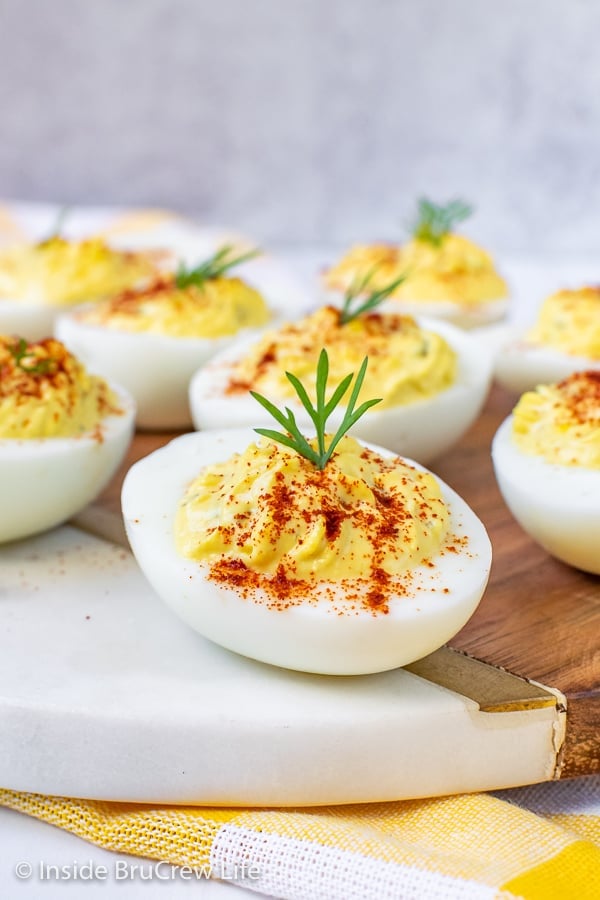 A close up picture of deviled eggs with a sprinkle of paprika and a sprig of dill on a white tray