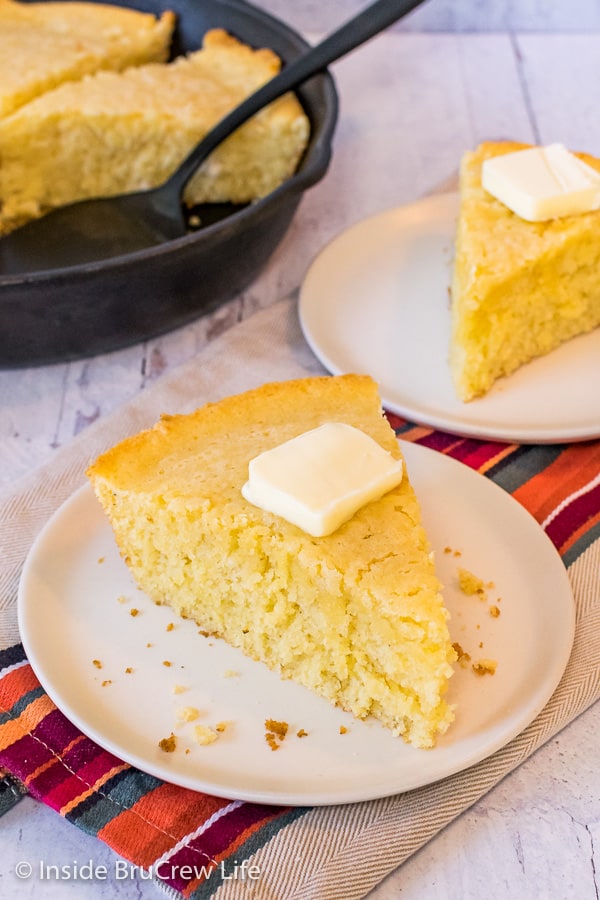 Slightly overhead picture of a wedge of skillet cornbread with a pat of butter on an off white plate