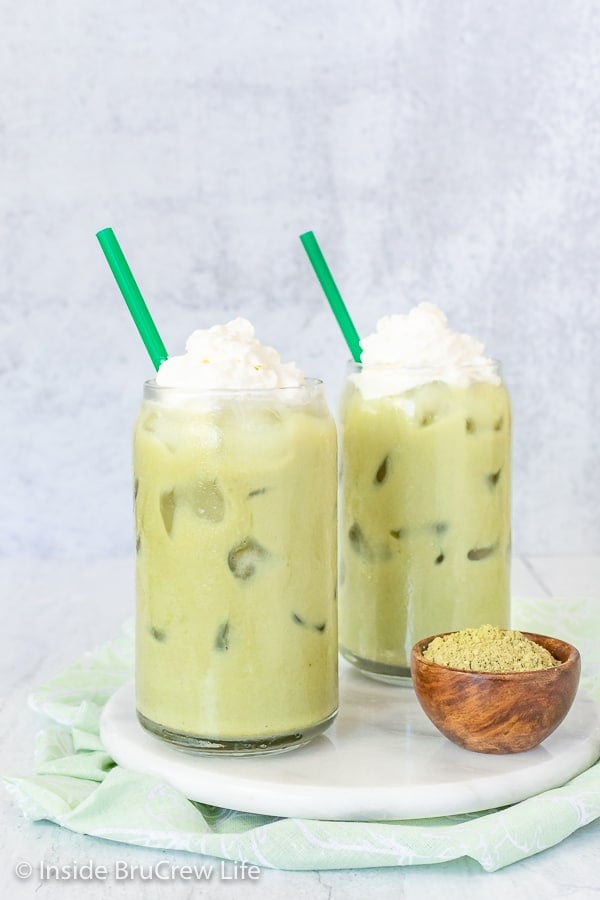 Two glasses of iced green tea with green straws on a white plate.