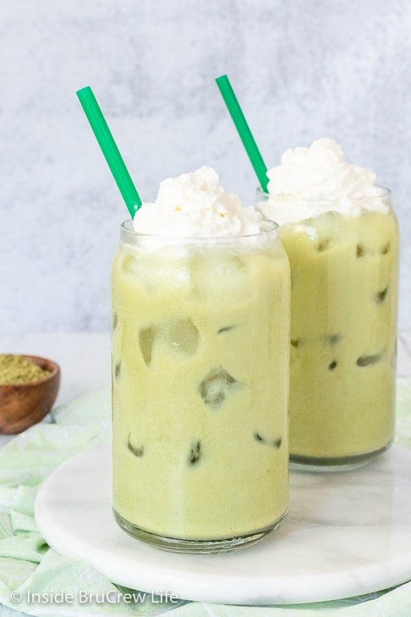Two green tea lattes with a green straw on a white plate.