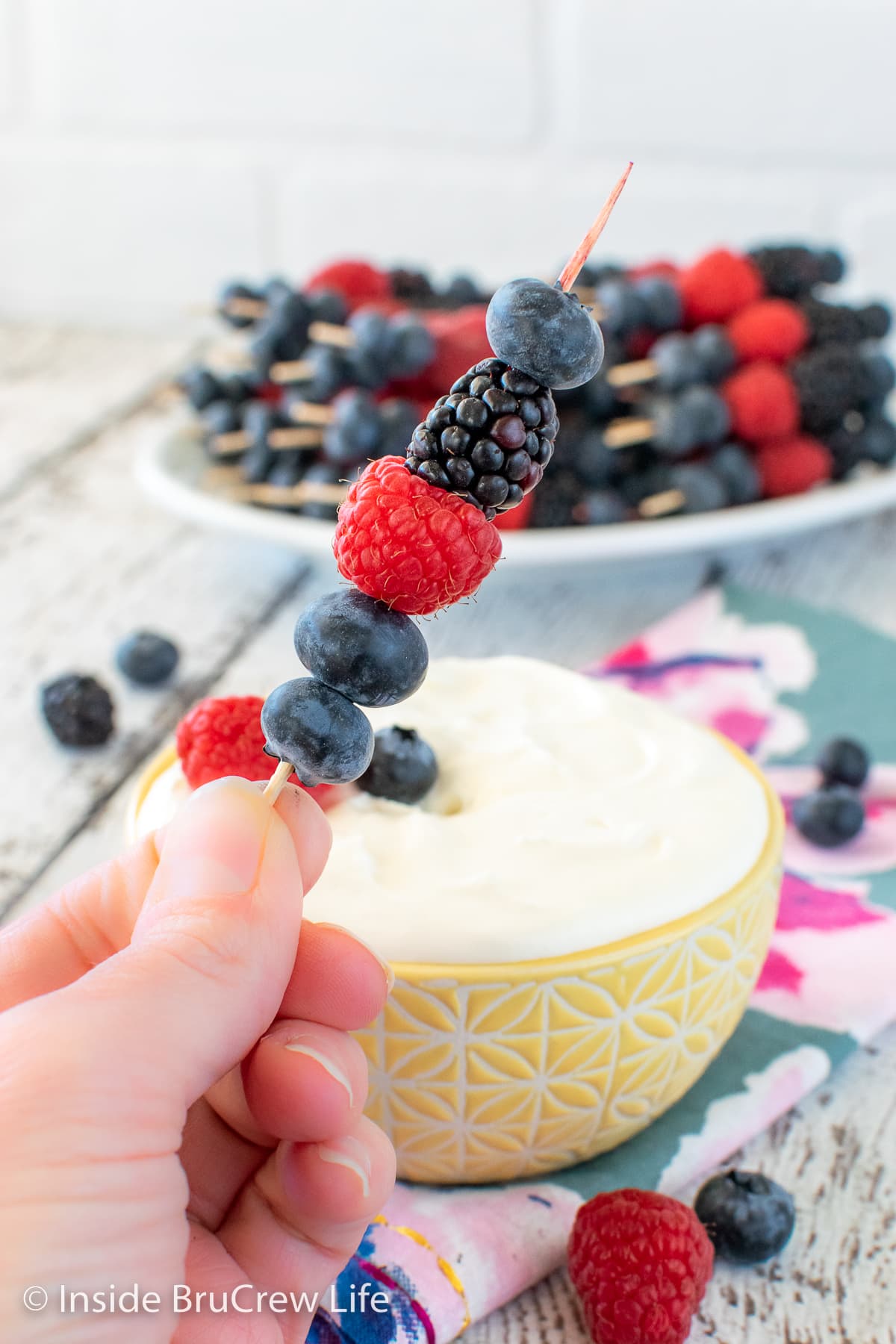 A bowl of fruit dip and fruit skewers.