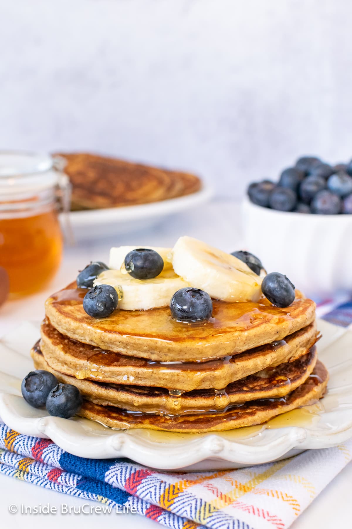 A stack of pancakes on a plate with blueberries and bananas.