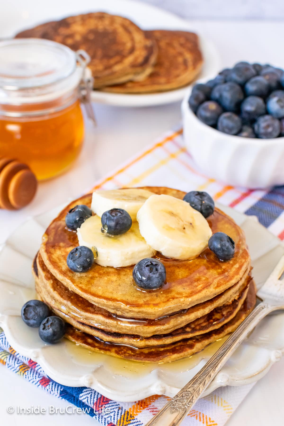 Pancakes on a white plate with blueberries and banana slices.