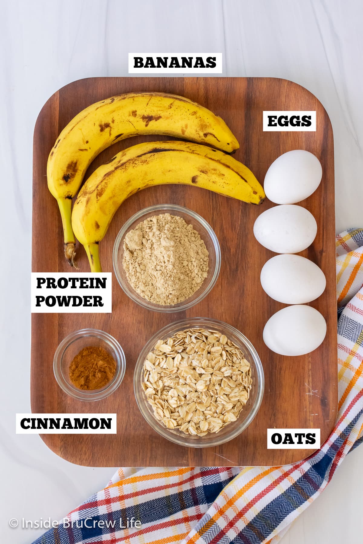 A brown board with bowls of ingredients needed to make banana egg pancakes.