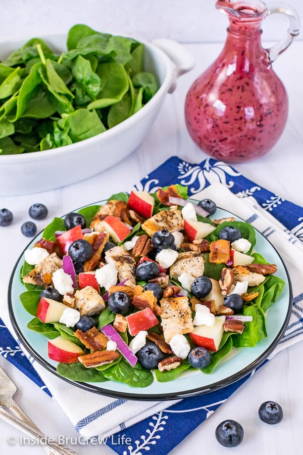 A blue plate on a blue towel topped with a spinach salad loaded with blueberries, nuts, cheese, and grilled chicken