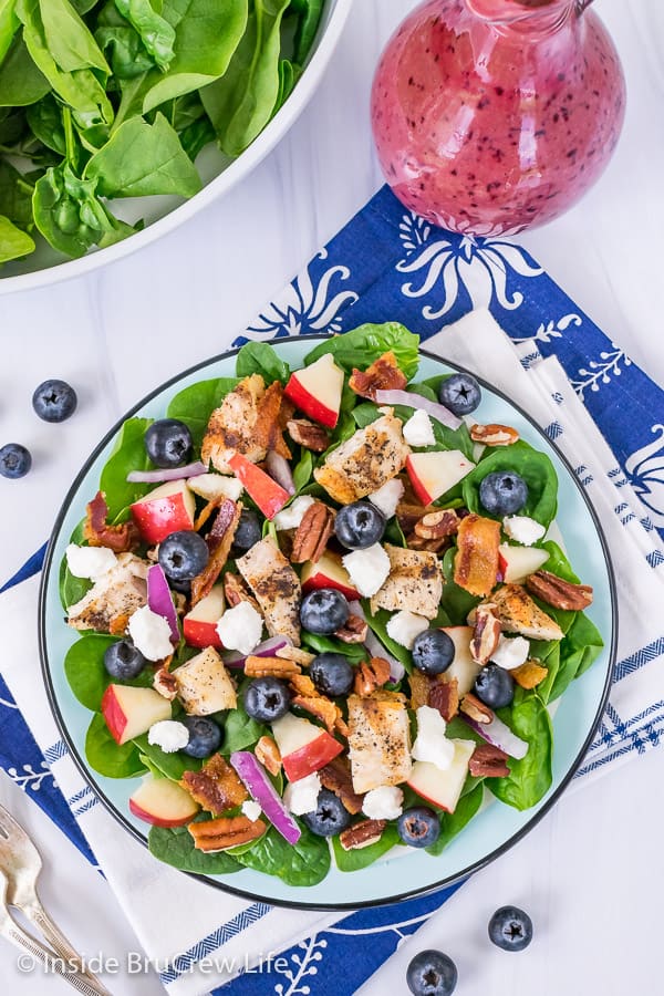 Overhead picture of a blue plate with a spinach salad topped with blueberries, apples, grilled chicken, nuts, and bacon