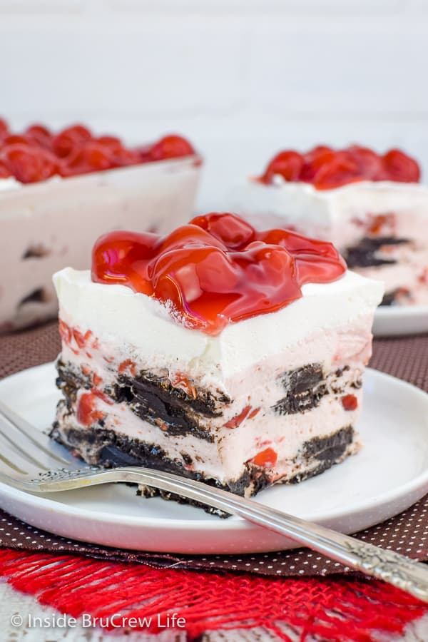 A square of cherry oreo icebox cake on a white plate with cherry pie filling on top and fork beside it