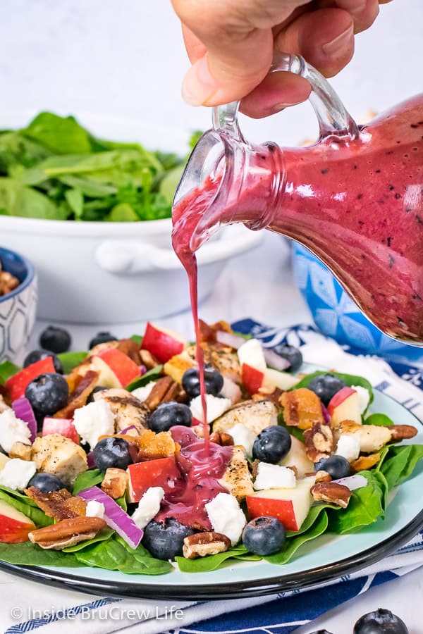 A jar of Blueberry Balsamic Salad Dressing being poured onto a spinach salad