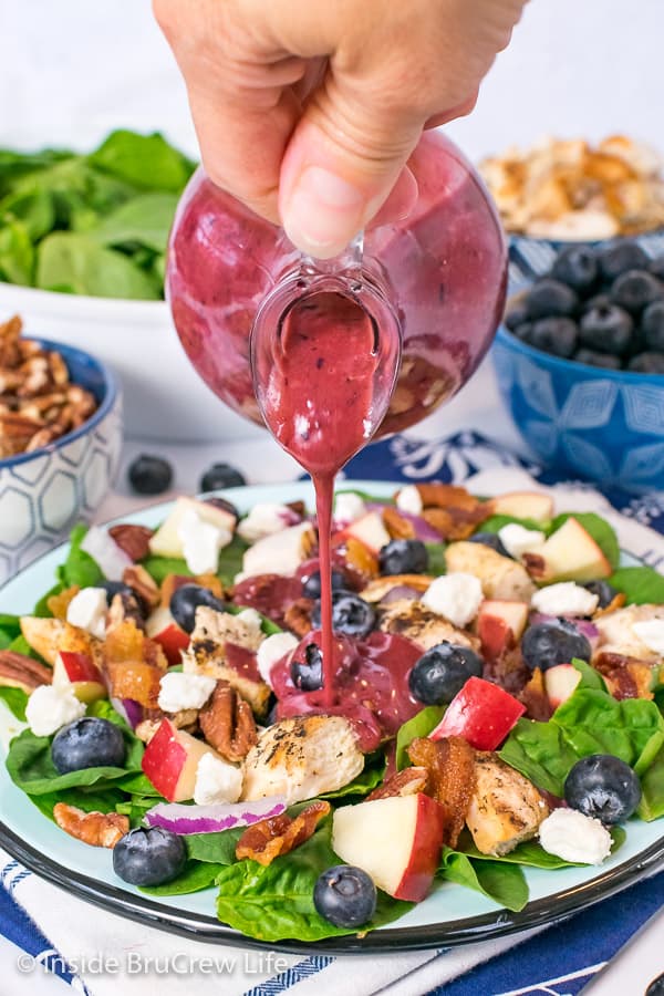 A jar of blueberry salad dressing being drizzled onto a plate of blueberry spinach salad 