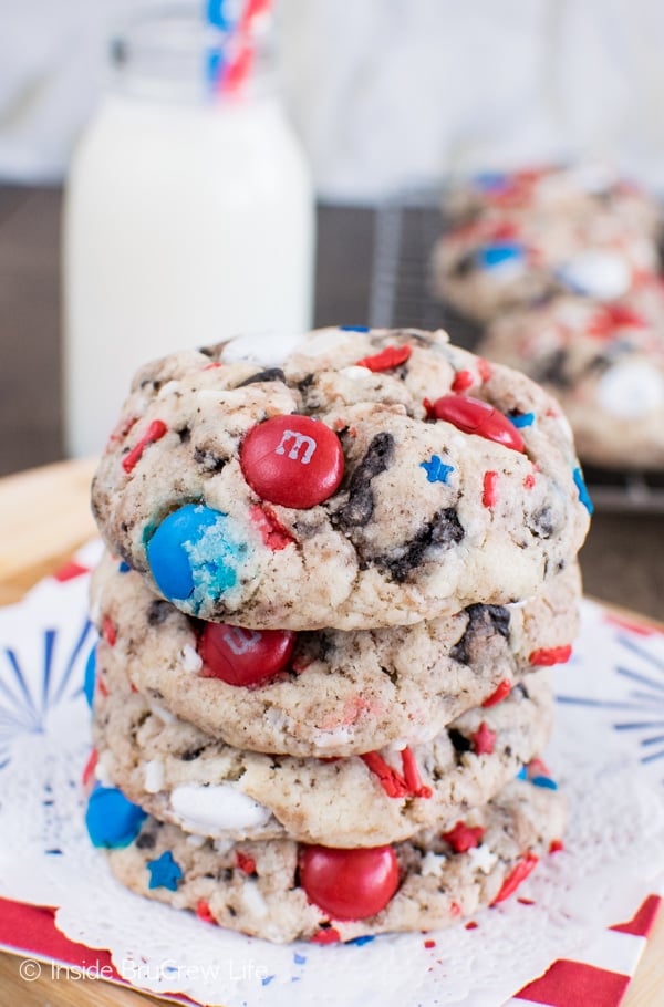 A stack of four Fireworks Cookies and Cream Cookies on a white doily with milk behind it