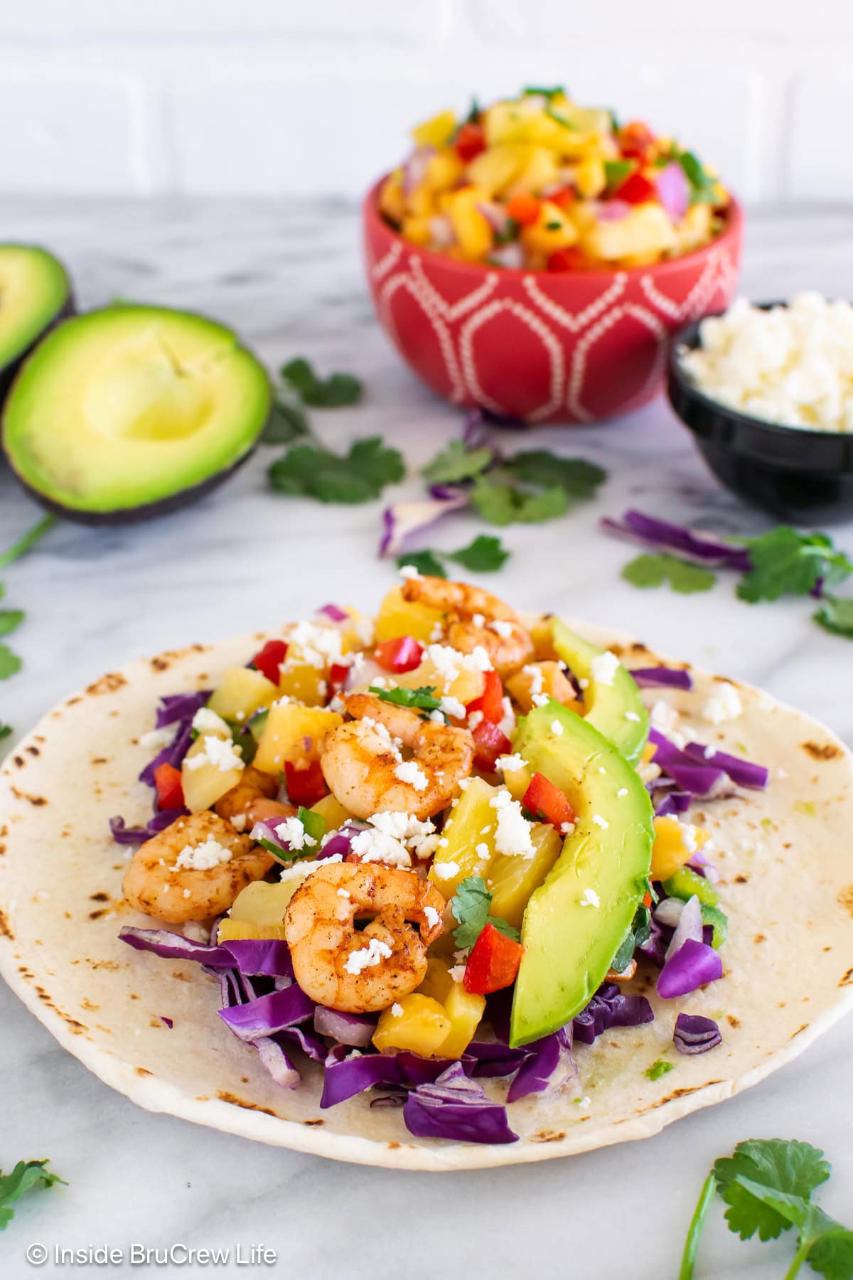 A flour tortilla on a white table filled with shrimp and toppings.