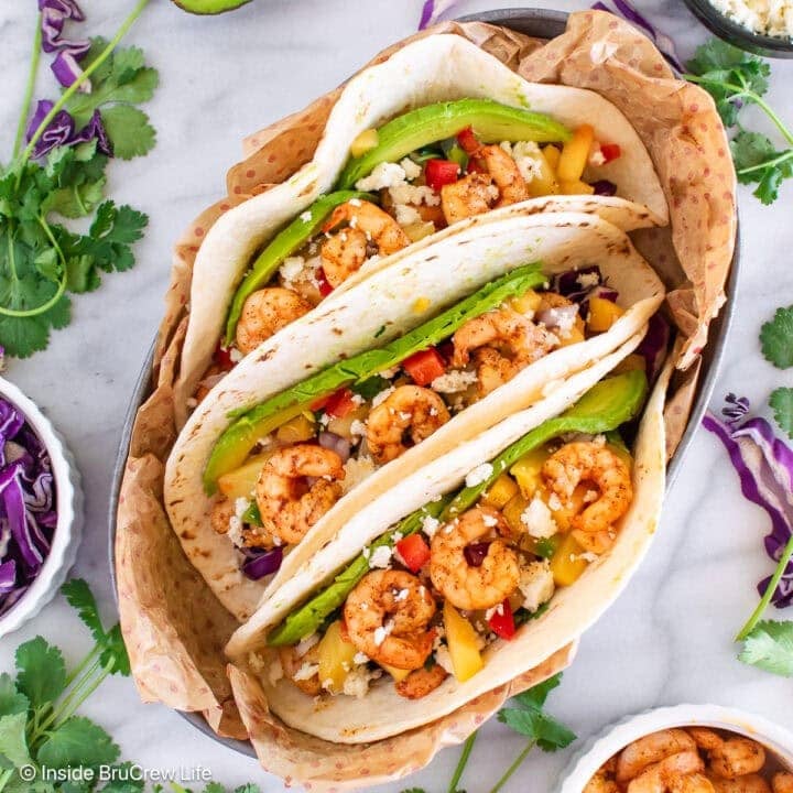 Three shrimp tacos with toppings in a serving dish.