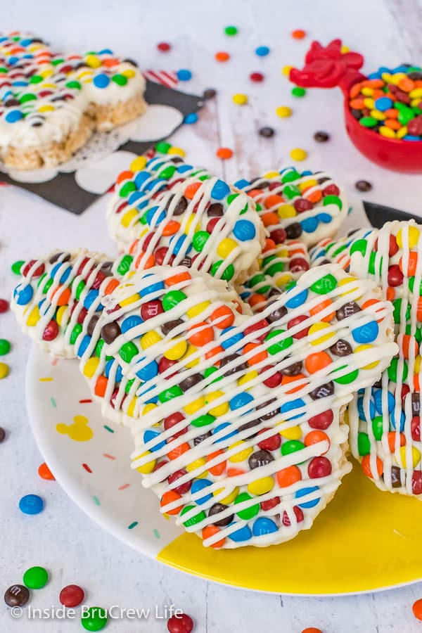 A close up picture of a plate of M&M's Mickey Mouse Rice Krispie Treats on a Disney plate with M&M's scattered around it