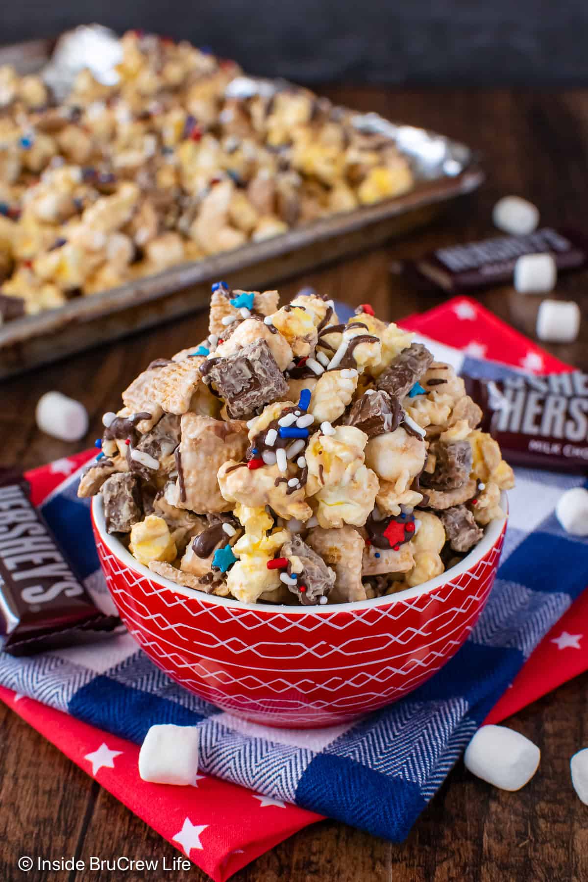 A bowl filled with s'mores popcorn and a pan behind it with more popcorn.