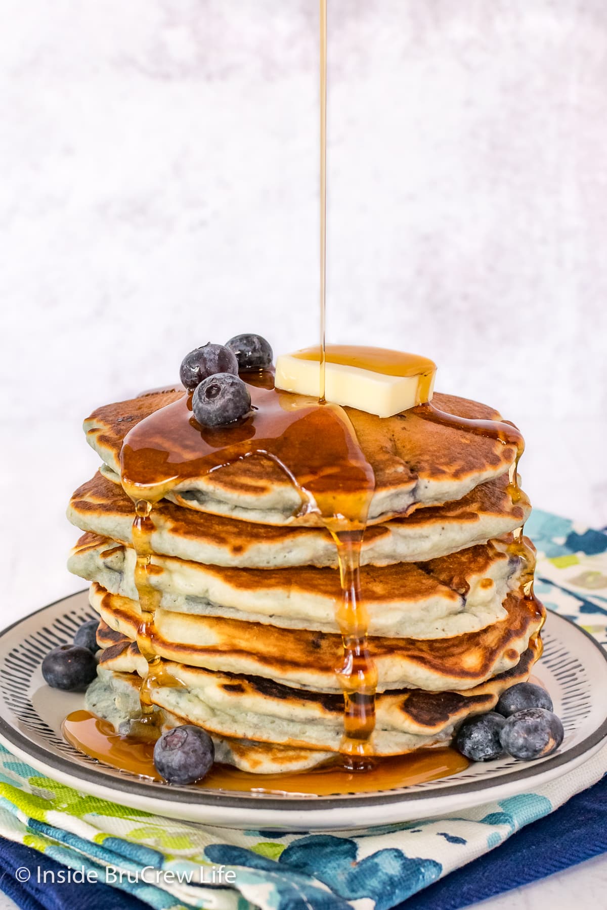 A stack of pancakes on a plate with a drizzle of syrup.