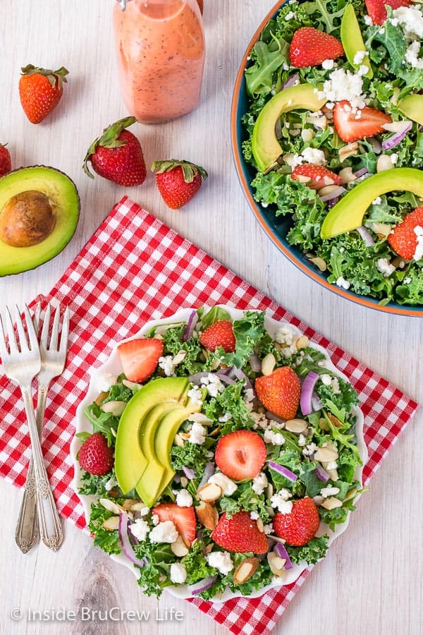 An overhead picture of a white plate filled with strawberry avocado salad and big bowl of salad beside it