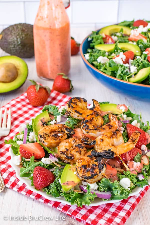 A white plate with strawberry avocado salad topped with grilled shrimp skewers