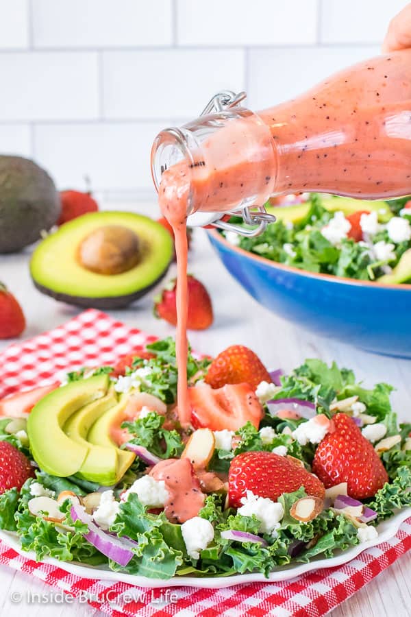 A plate of salad with a bottle of strawberry poppy seed salad dressing being drizzled over it