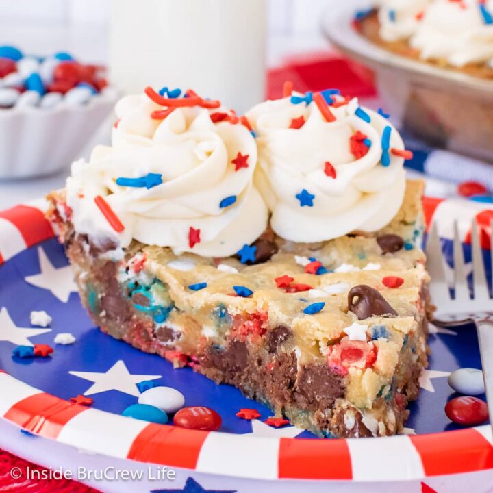 A slice of cookie cake with frosting and red white and blue sprinkles on a plate.