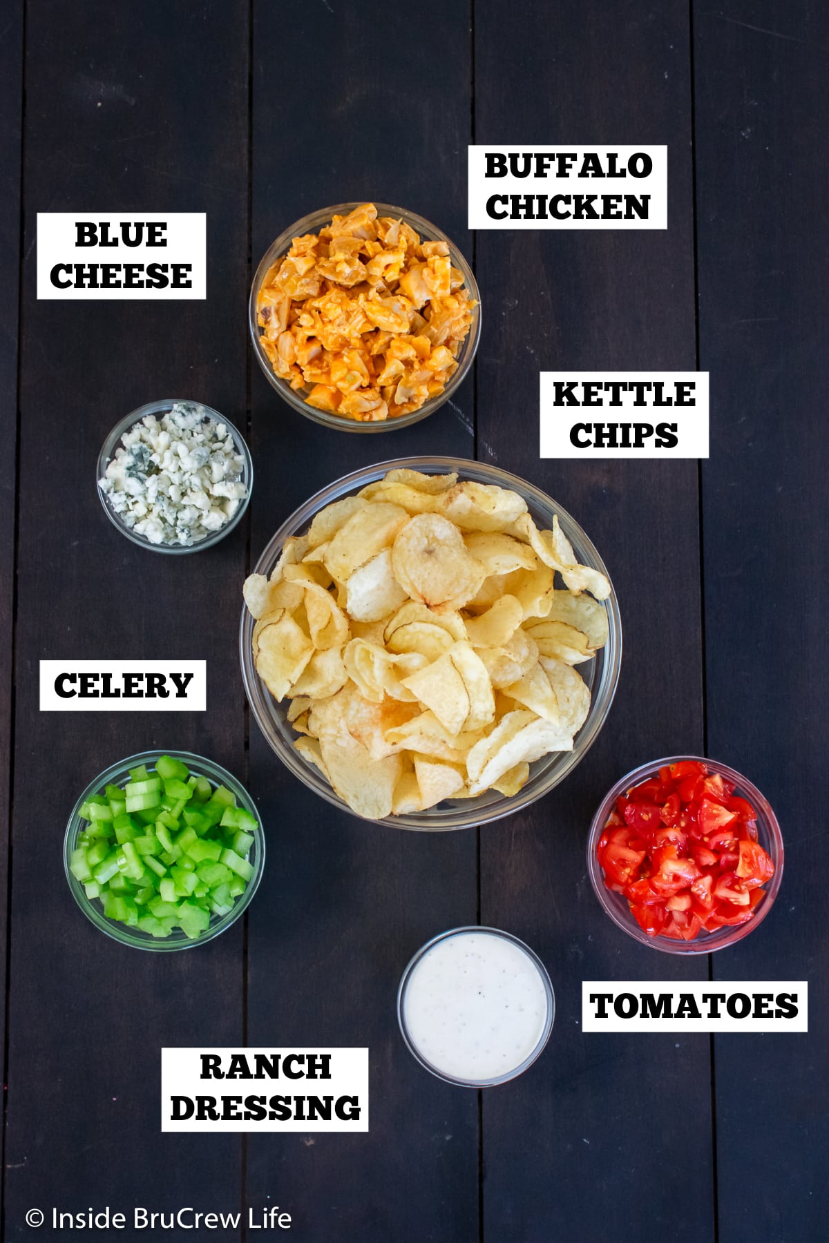 A dark board with bowls of ingredients needed to make kettle chip nachos.
