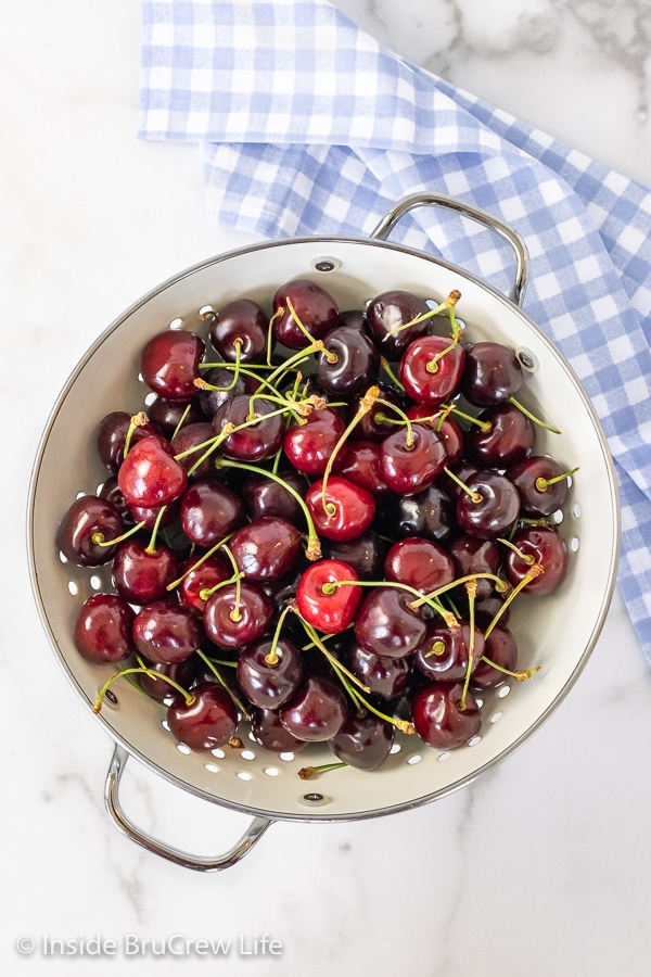 Overhead picture of a white board with a white colander filled with fresh cherries with stems