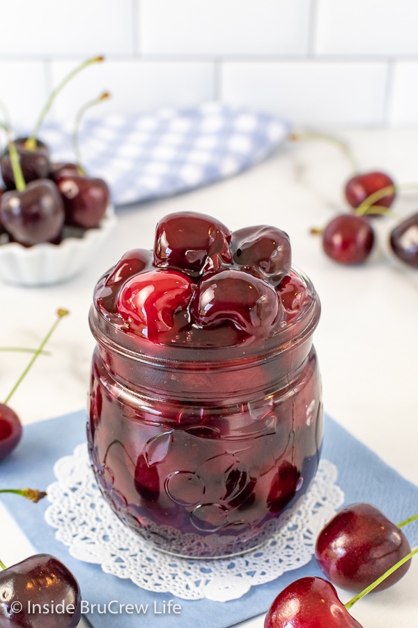 A clear jar filled with homemade cherry pie filling with fresh cherries around it