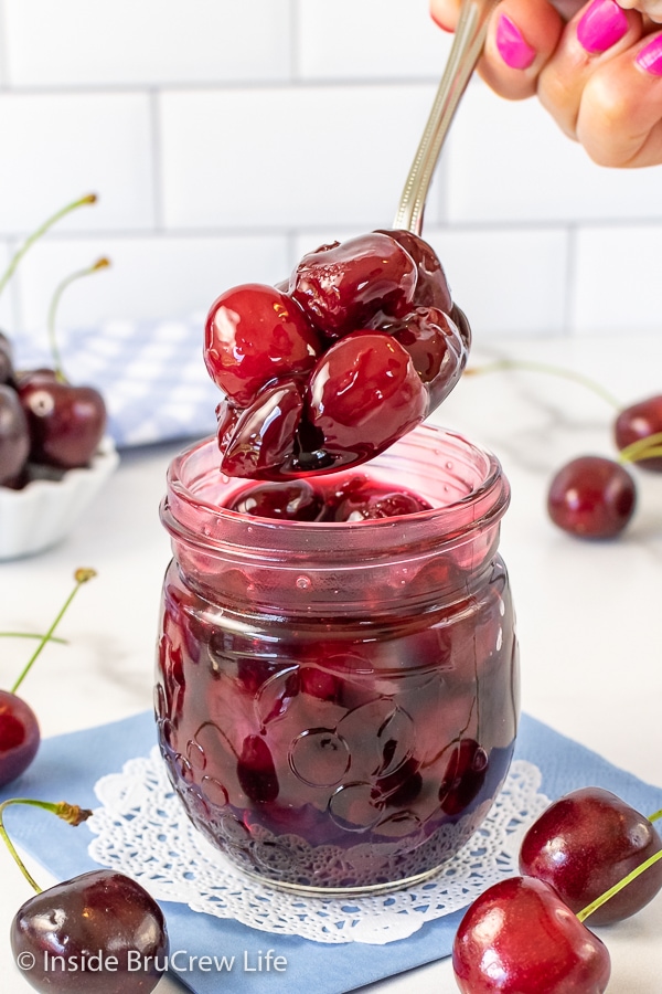 A clear jar of cherry pie filling with a spoon lifting out a spoonful of filling.