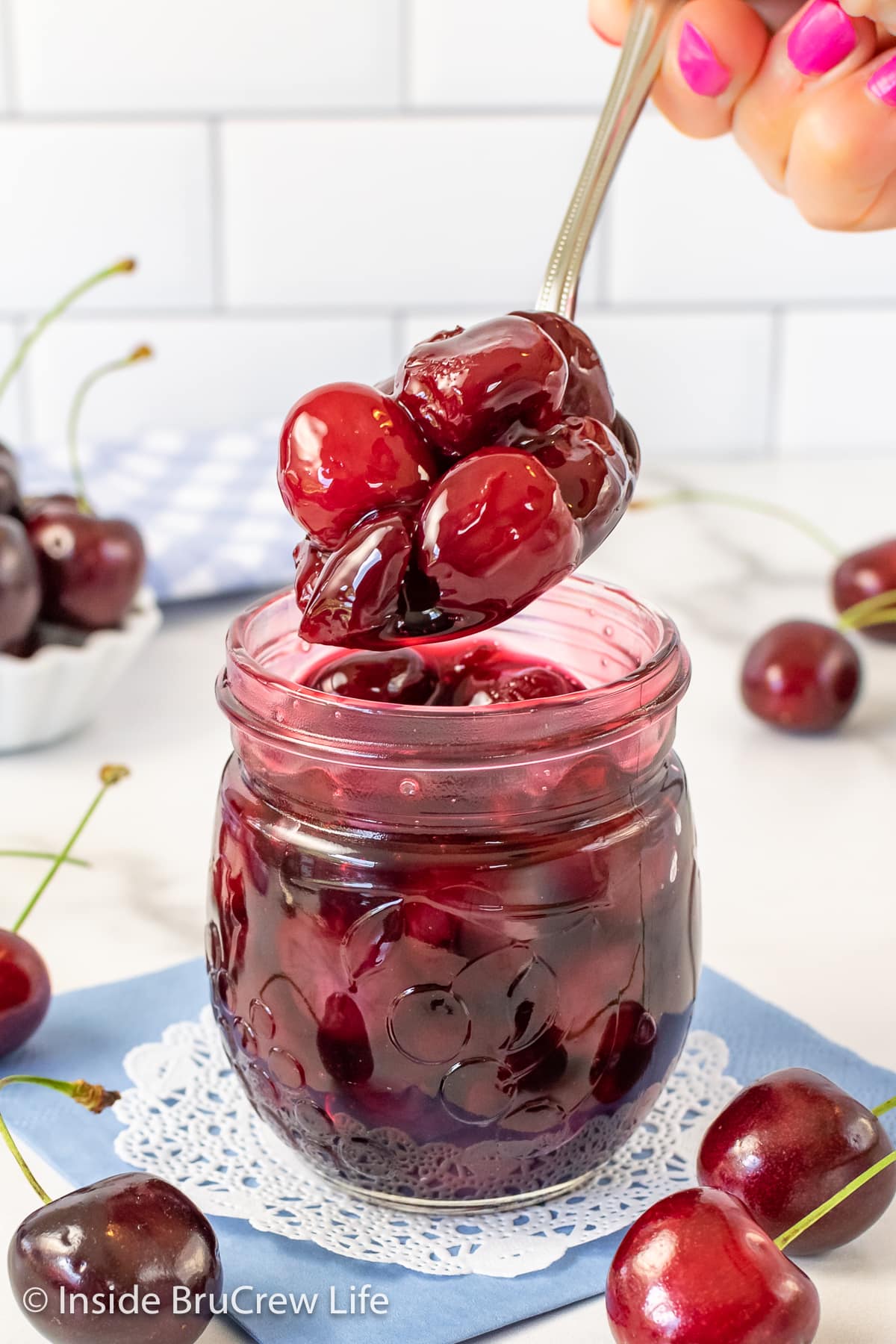 A clear jar of cherries with a spoon lifting them out.