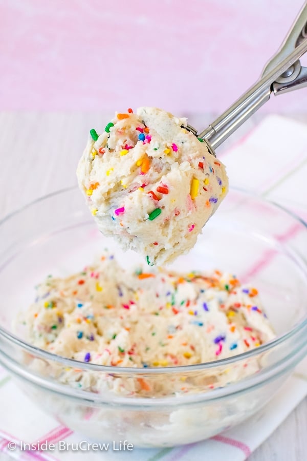 A bowl of cookie dough with a cookie scoop lifting up a big spoonful.
