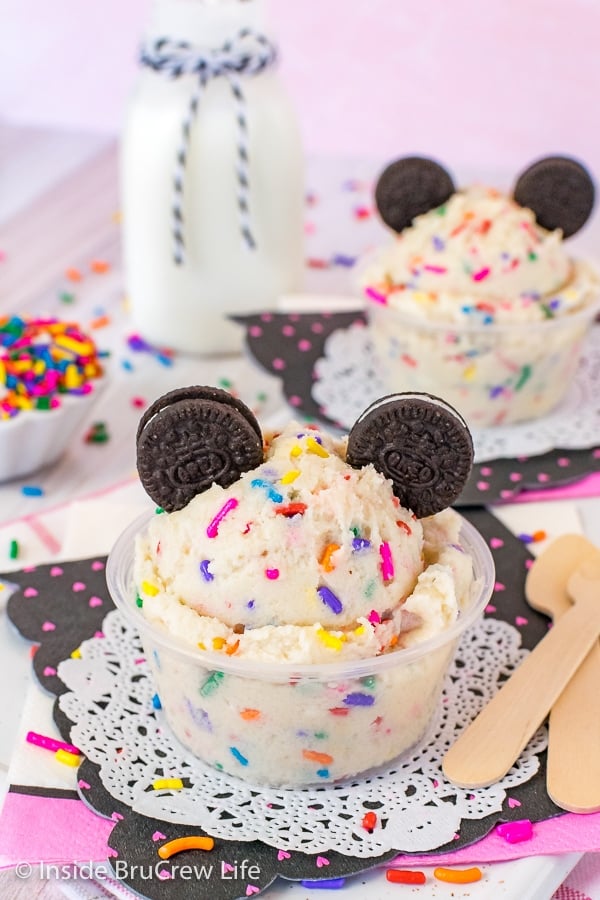 Two clear cups filled with cookie dough loaded with colorful sprinkles and topped with chocolate cookies.