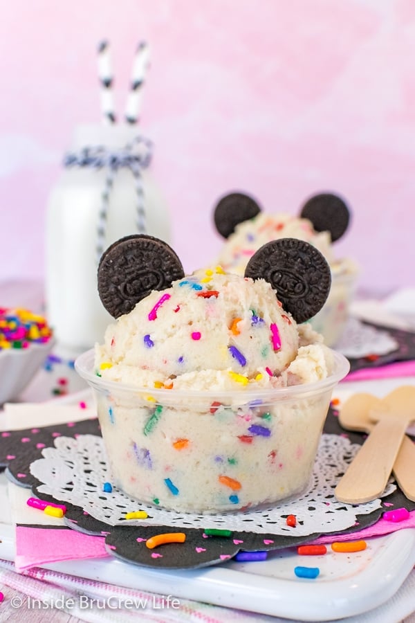 A clear cup filled with cookie dough and topped with two chocolate cookies making it look like Mickey Mouse.