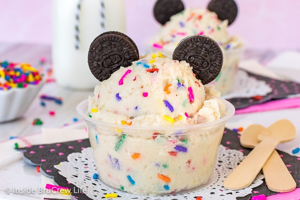 A clear cup filled with cookie dough loaded with colorful sprinkles and topped with chocolate cookies.