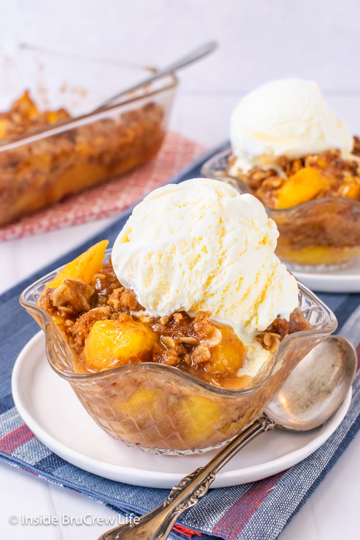 A clear bowl of peaches with oat topping and ice cream.