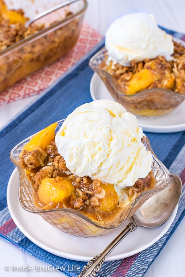 A clear bowl on a white plate filled with peach crisp and vanilla ice cream