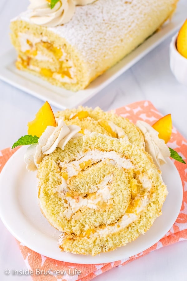 A white plate with two slices of peaches and cream cake roll on it facing up