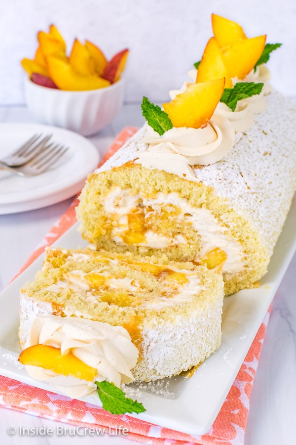 A peaches and cream cake roll on a white plate with one slice flipped down