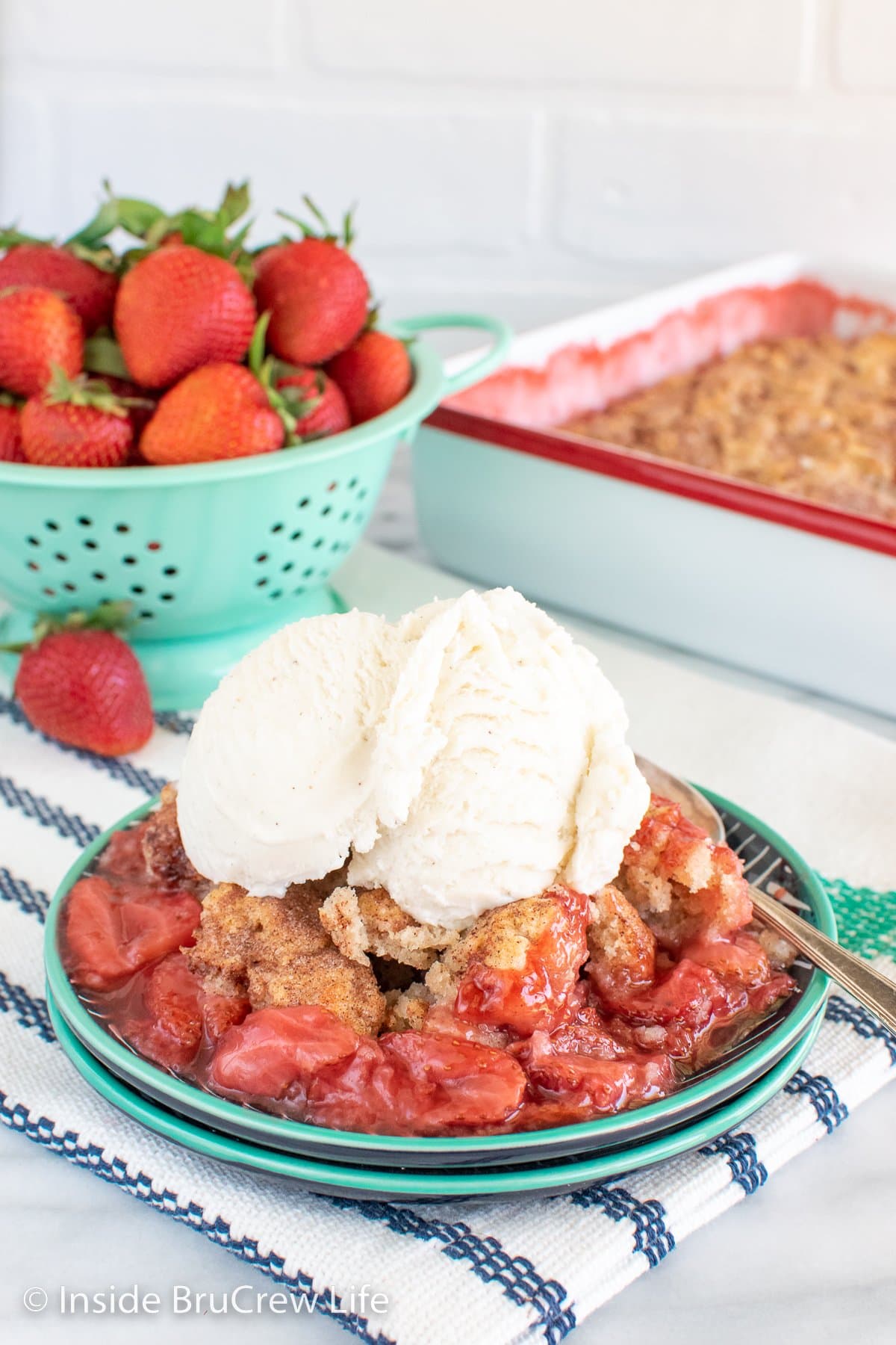 Strawberry cobbler topped with vanilla ice cream on a plate.