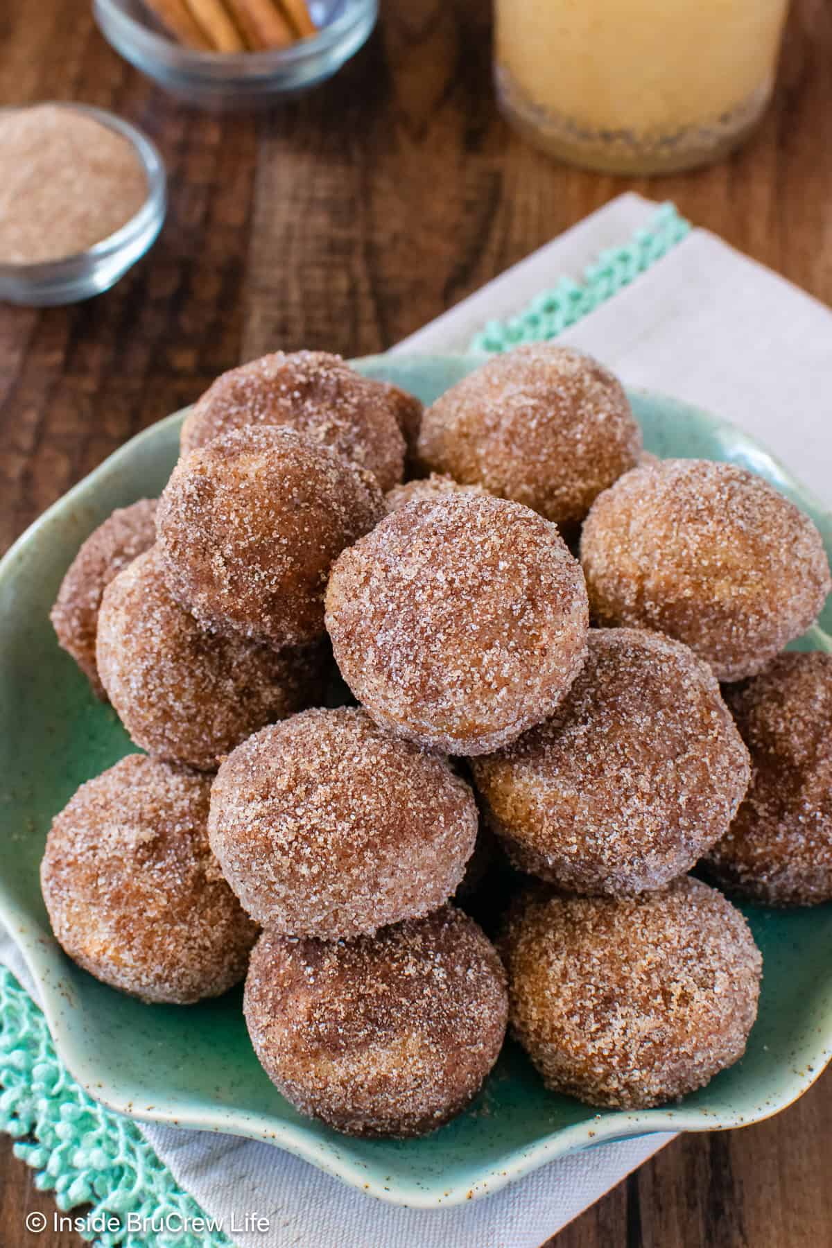 Apple Cider Donut Holes - a buttery cinnamon sugar coating makes these apple donuts a delicious treat. Make this easy fall recipe for breakfast or an after school snack. A green plate with apple cider donut holes piled on it.