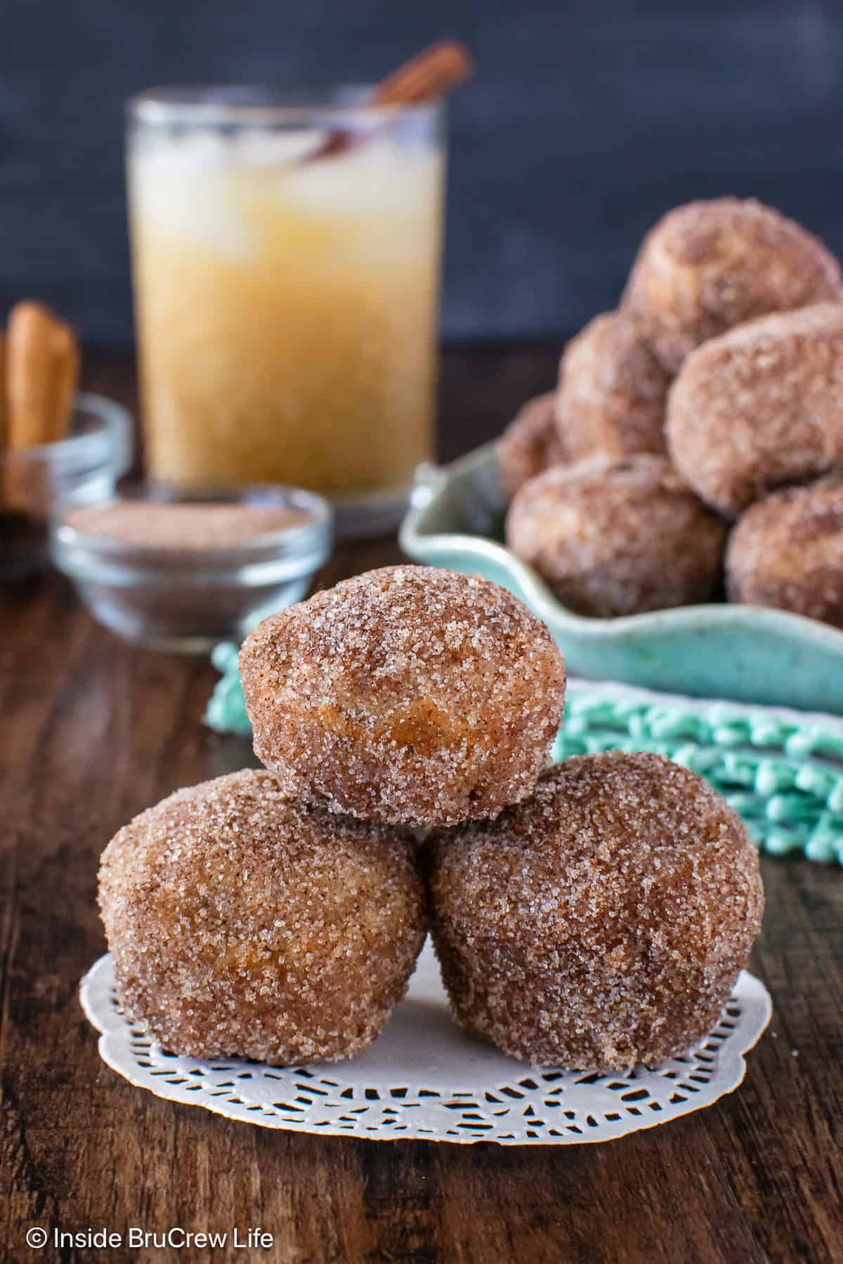 Apple Cider Donut Holes - three times the apple goodness makes these homemade apple donuts the best fall treat! Make this easy recipe for breakfast or an after school snack. Three cinnamon sugar apple cider donuts stacked on a wooden board.