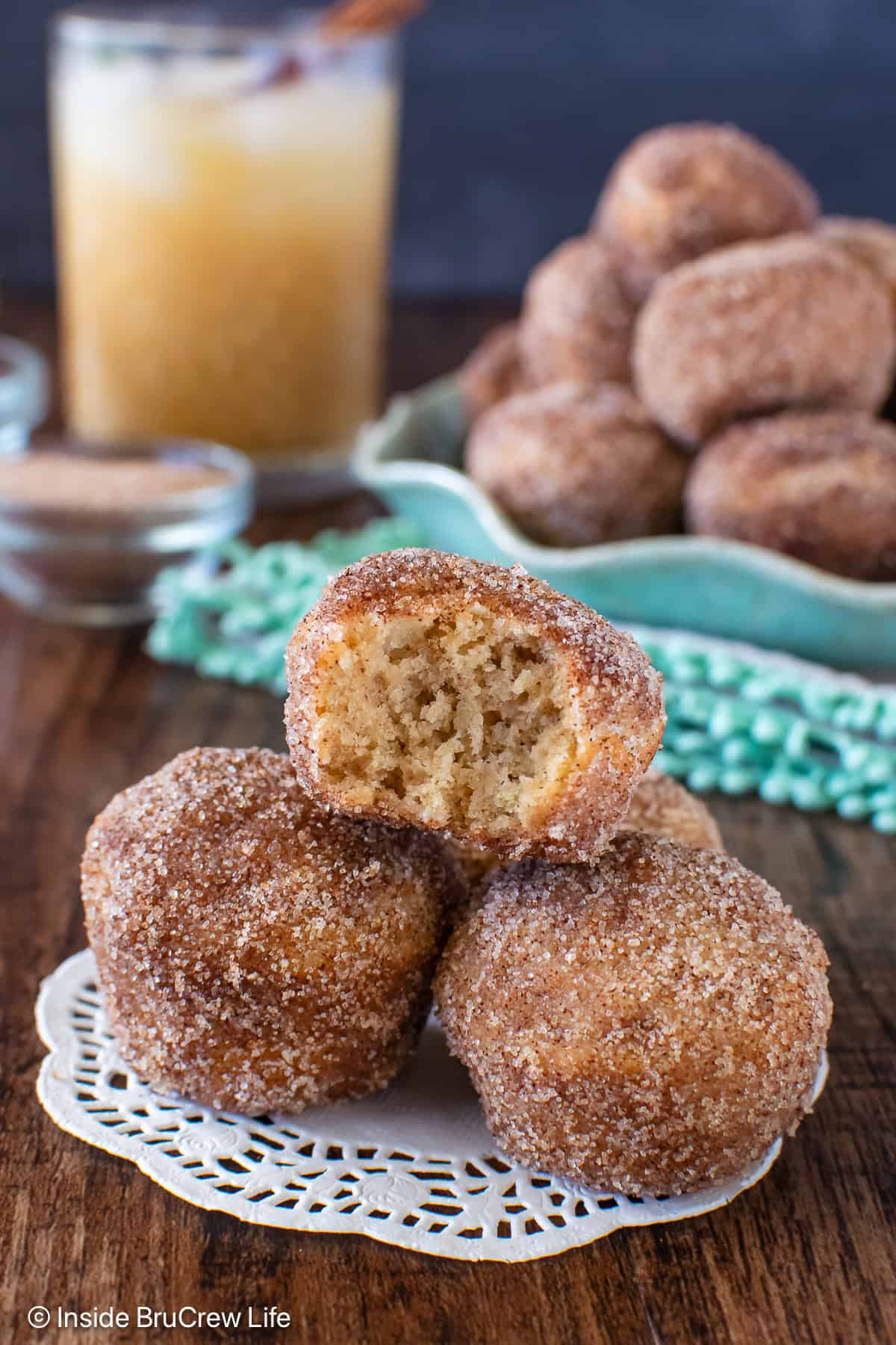 Apple Cider Donut Holes - the crunchy cinnamon sugar coating makes these apple donuts so delicious! Awesome fall breakfast recipe! Three apple cider donuts stacked on a board with a bite out of the top one.