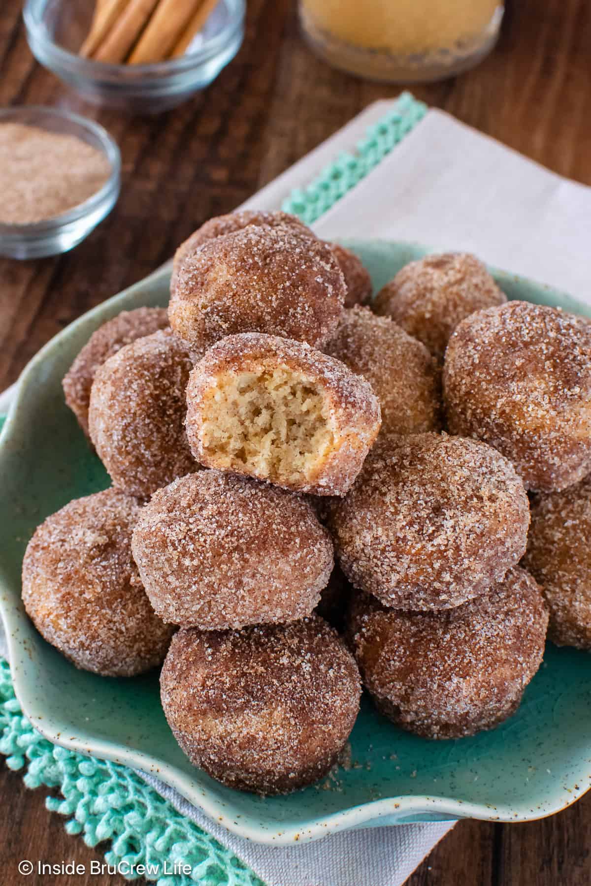 Apple Cider Donut Holes - three times the apple goodness and the crunchy coating make these donut holes disappear in a hurry. Make this easy breakfast recipe for fall mornings! A plate of cinnamon sugar apple cider donut holes with one missing a bite.