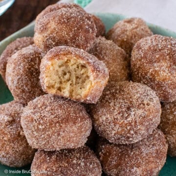 A plate of cinnamon sugar apple cider donut holes with one missing a bite.