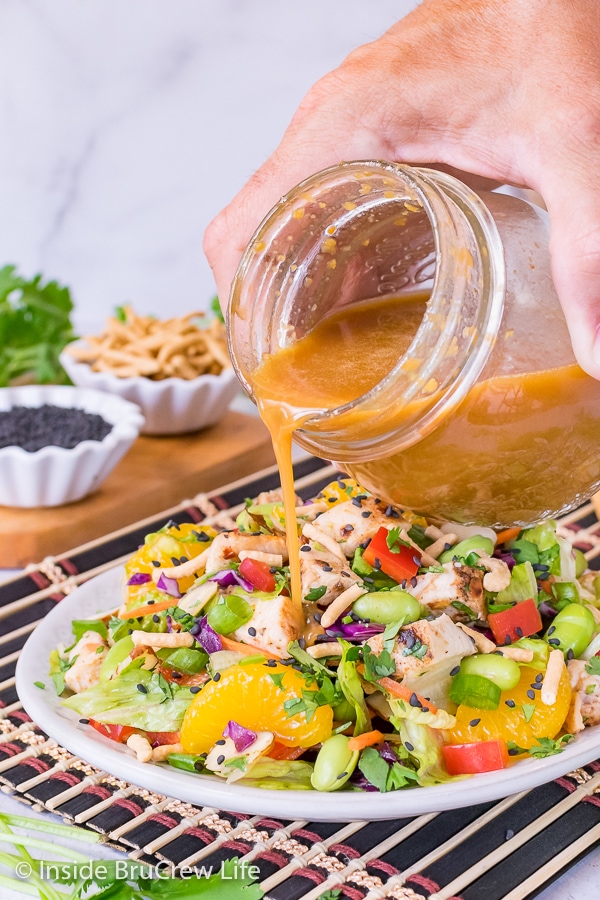 A jar of homemade Asian salad dressing being drizzled onto a plate of Asian Chicken Salad.