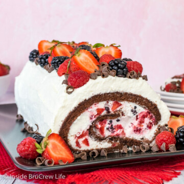 A full berries and cream chocolate cake roll on a black plate showing the inside swirl of cream and berries